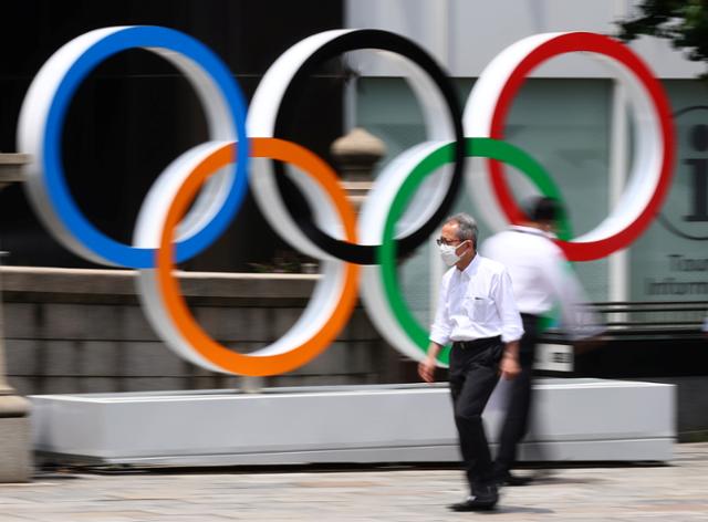 마스크를 쓴 한 남성이 28일 도쿄의 올림픽 조형물 앞을 지나가고 있다. 이날 도쿄에서는 코로나19 신규 감염자 수가 이틀째 최다 기록을 경신했다. 도쿄=로이터 연합뉴스