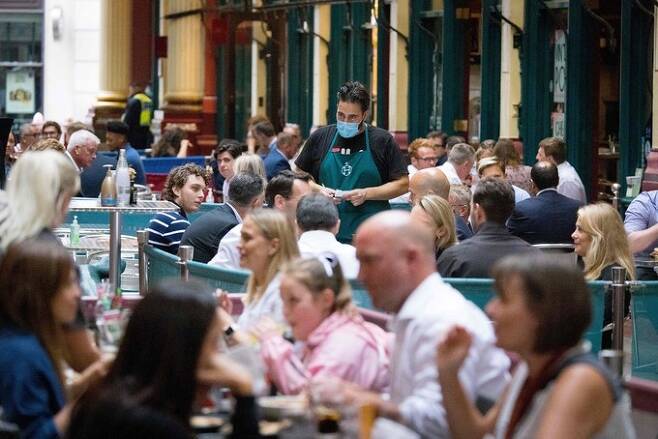 27일(현지시간) 영국 런던의 한 식당에서 종업원이 마스크를 쓴 채 주문을 받고 있다. 그를 제외한 다른 사람들은 마스크를 쓰지 않은 모습이 눈에 띈다. 런던=AFP연합뉴스