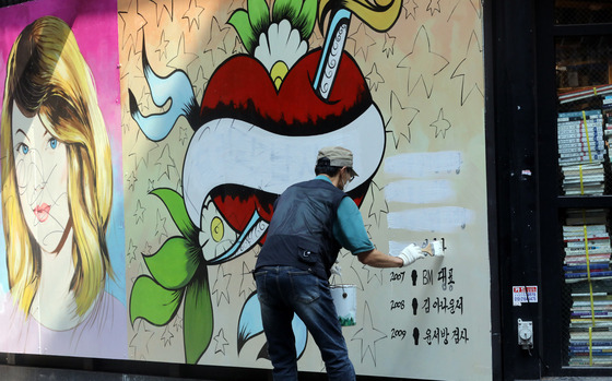 A mural entitled “Julie's men” painted on a bookstore wall in Jongno District, central Seoul, seen to be disparaging former Prosecutor General Yoon Seok-youl’s wife, has been receiving backlash from Yoon’s supporters. A man covers up the list of high-profile men she has been rumored involved with in the past with white paint Friday. [NEWS1]