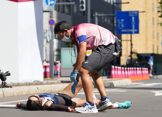 A staff member helps Choi Kyung-sun on the ground during the women's marathon final at the Tokyo 2020 Olympic Games in Sapporo, Japan on Saturday. [Xinhua/YONHAP]