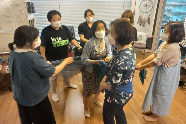 ▲ 돌봄전담사가 처한 상황을 형상화한 채 사회극을 진행하고 있는 모습. 돌봄전담사 역을 맡은 참가자는 아이 역을 맡은 참가자의 허리에 파란 끈을 두르고 잡고 있다. 전담사 역을 맡은 참가자의 허리에는 가지각색의 끈이 둘러져 있다. 그 주변에 학부모, 교사, 교장, 교육청 공무원 등 역할을 맡은 참가자들이 전담사의 허리에 둘러진 끈을 잡고 있다. 전담사는 돌봄교실에서 마주치는 많은 사람으로부터 압박을 받는 가운데 아이를 돌본다. ⓒ프레시안(최용락)