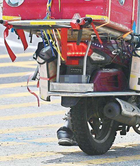 - 도로를 주행 중인 한 배달 오토바이의 번호판이 설치물과 액세서리에 가려 잘 보이지 않는다.