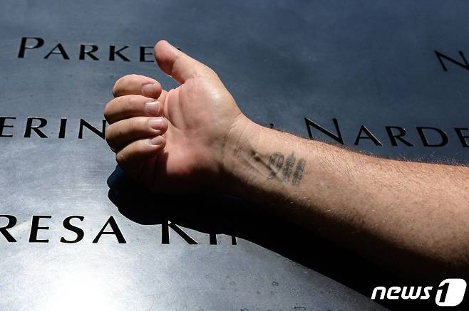 8일(현지시간) 911 테러 생존자인 조셉 디트마르가 세계무역센터 자리에 마련된 911 추모 공원 앞 기념비 위에 '911' 글자를 새긴 자신의 오른 손목을 드러내 보이고 있다. 당시 그는 세계무역센터 105층에서 근무를 하고 있었다. 2021.06.08 © AFP=뉴스1