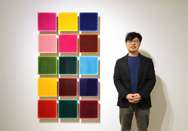 화면에 무수한 선을 그어 심오한 공간을 표현하는 작품 `Who likes YJ color?` 연작 옆에 서 있는 김현식 작가. [사진 제공 = 학고재 갤러리]