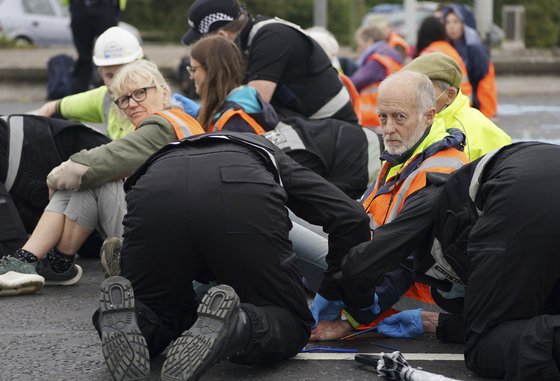 지난 20일 적극적인 기후 위기 대응을 촉구하는 시위를 벌인 영국 노인들. 고속도로 위에 앉아 차량 통행을 막았다. 바닥에 접착제로 붙여 놓은 한 노인의 손을 경찰이 떼어내고 있다. [AP=연합뉴스]