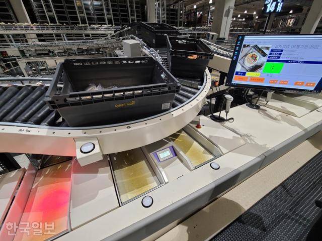 GTP 설비 작업대의 모습. 사람이 서 있는 곳에 재고 바구니가 도착해 있다. 오른쪽 화면에 적힌 개수만큼 상품을 꺼내 품질, 유통기한을 확인한 뒤 불빛이 들어온 곳에 놓으면 된다. 조소진 기자