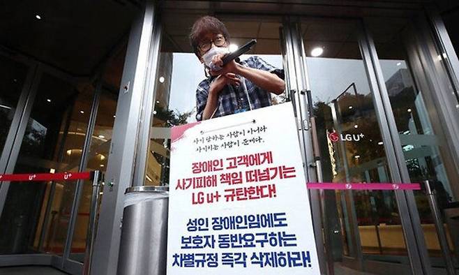 장애인단체 관계자가 지난달 7일 서울 용산구 LG유플러스 본사 앞에서 장애인 차별 규정에 항의하는 시위를 하고 있다. 연합뉴스