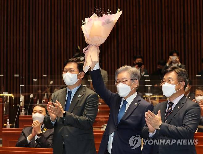 꽃다발 들어올린 이재명 후보 (서울=연합뉴스) 전수영 기자 = 이재명 대선 후보가 15일 오전 서울 국회에서 열린 더불어민주당 의원총회에 참석해 송영길 당대표(왼쪽), 윤호중 원내대표(오른쪽)와 함께 포즈를 취하고 있다. 2021.10.15 [국회사진기자단] swimer@yna.co.kr