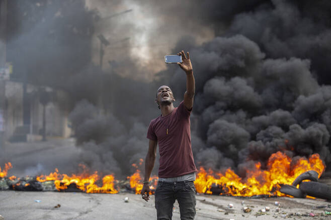 18일 아이티 수도 포르토프랭스에서 한 시위 참여자가 불타는 타이어를 배경으로 ‘셀피’를 찍고 있다. 포르토프랭스/AP 연합뉴스