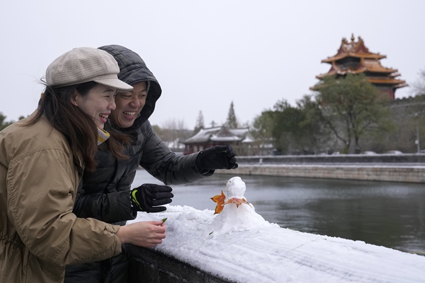 7일 중국 자금성(고궁박물관)을 찾은 관광객이 첫눈으로 만든 눈사람에 가을 단풍을 올리고 있다./AP연합뉴스