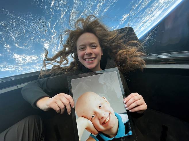 우주선의 전방 해치를 열면 우주선 역사상 가장 큰 규모의 큐폴라 유리창이 등장한다. 우주에 간 최초의 소아암 생존자 헤일리가 투병 시절 사진을 들고 있다./넷플릭스