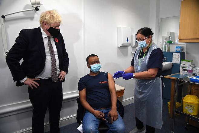 보리스 존슨 영국 총리(왼쪽)가 지난 15일(현지시각) 런던 동부의 백신 접종센터에서 한 시민이 신종 코로나바이러스 감염증(코로나19) 백신을 추가접종(부스터샷) 받는 모습을 지켜보고 있다./연합뉴스