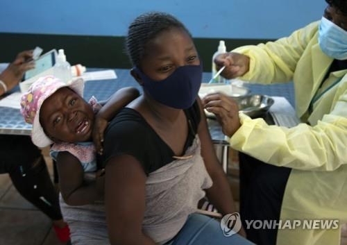 남아프리카 공화국 요하네스버그에서 아이를 업은 한 여성이 코로나19 백신을 접종하고 있다.   AP/연합뉴스