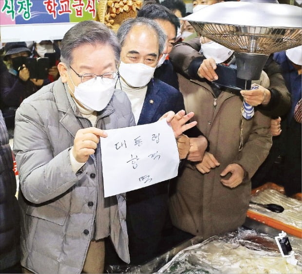 < ‘대통령 합격 떡’ 산 이재명 > 이재명 더불어민주당 대선 후보(왼쪽)가 5일 전북 정읍 샘고을시장에서 떡을 산 뒤 ‘대통령 합격 떡’이라고 적힌 종이를 들어 보이고 있다.  뉴스1