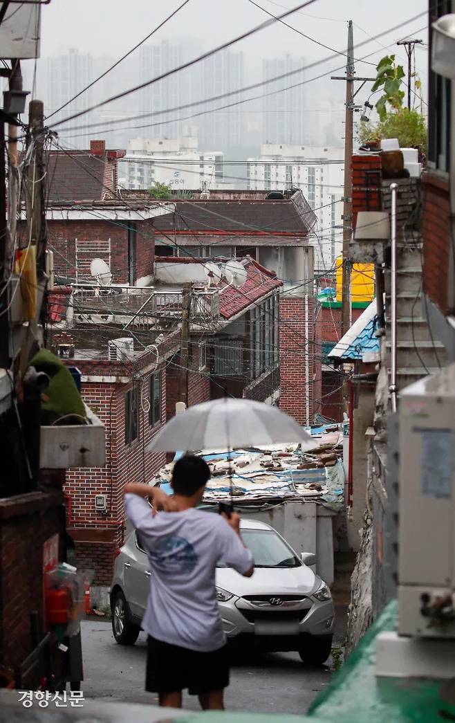 비 내리는 서울 용산구 주택가 골목길을 한 시민이 걸어가고 있다. 멀리 강남 쪽에 아파트들이 늘어서 있다. 이준헌 기자 ifwedont@kyunghyang.com