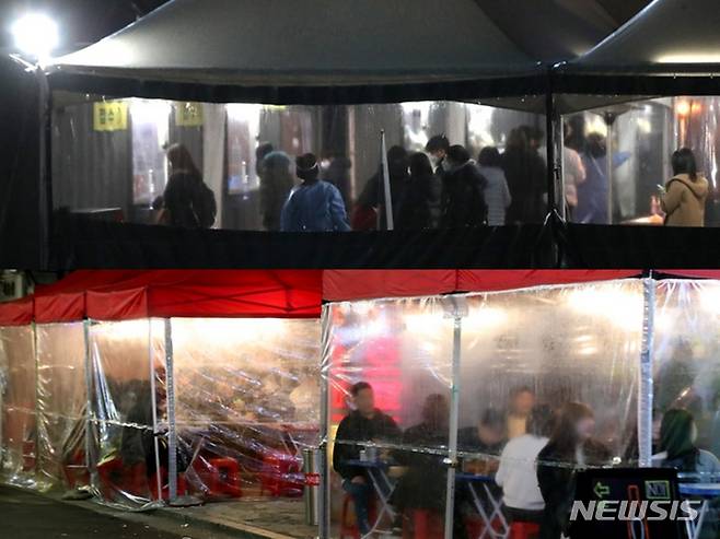 [서울=뉴시스] 조수정 기자 = 0시 기준 코로나19 신규 확진자수가 일일 7000명을 넘긴 8일 밤 서울 중구 서울광장 코로나19 임시선별검사소에서 시민들이 늦은 시간 코로나19 검사를 받기 위해 줄서 기다리고 있다.(위쪽) 서울 시내 한 먹자골목 맥주집에서 시민들이 저녁 시간을 즐기고 있다.(아래쪽) 2021.12.08. chocrystal@newsis.com
