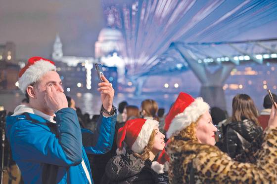 산타클로스 모자를 쓴 사람들이 지난 1일 런던 밀레니엄브리지에서 새해맞이 빛축제를 즐기고 있다. [AP=연합뉴스]