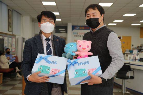 건보 관계자(왼쪽)이 세쌍둥이 아버지에게 건이강이 캐릭터 인형과 육아용품을 선물하고 있다.