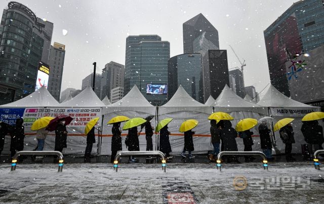 눈이 내리는 19일 서울 서초구 강남역 임시선별검사소에서 검사를 받기 위해 방문한 시민들이 우산을 쓴 채 줄지어 서 있다.