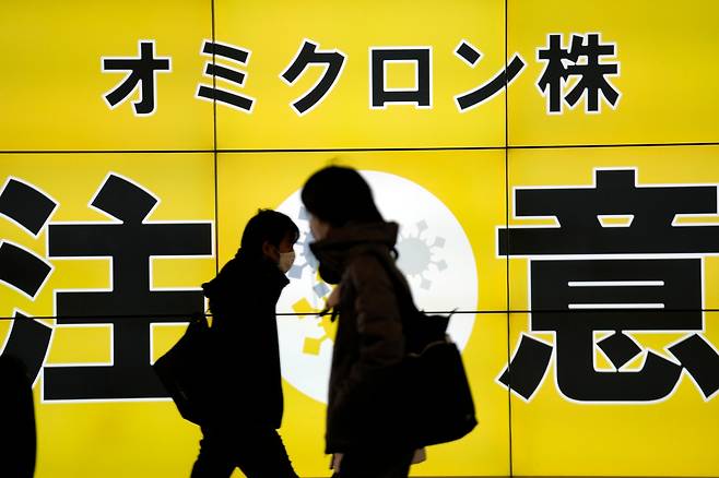 지난 24일 일본 수도 도쿄 거리에서 마스크를 쓴 행인이 신종 코로나 바이러스 오미크론 변이 확산에 주의하라는 내용의 공공 안내판 앞을 지나고 있다. /교도연합뉴스