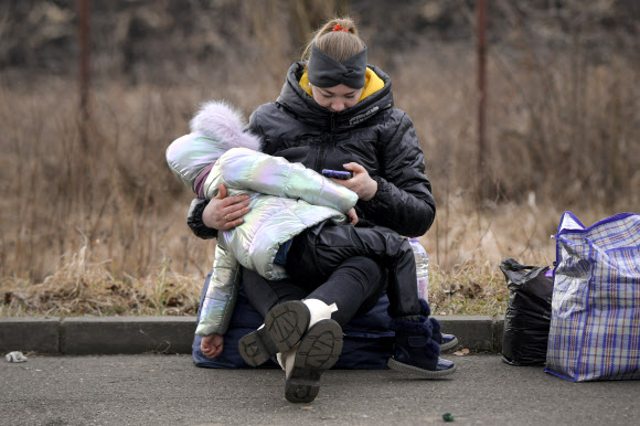 엄마 품에서 지쳐 잠든 우크라이나 아이 - 2022년 2월 27일 일요일 루마니아 시레트의 루마니아-우크라이나 국경에서 이웃 우크라이나에서 온 난민들이 수송을 기다리고 동안 지친 아이가 엄마 품에 잠들어 있다. 러시아가 우크라이나에 대한 공세를 시작한 이후, 20만 명 이상의 사람들이 루마니아, 폴란드, 헝가리, 몰도바, 체코 공화국과 같은 국경 국가들로 우크라이나를 떠나야만 했다.유엔난민기구인 유엔난민기구(UNHCR)는 민간인들에게 “인도주의적 결과를 파괴할 것”이라고 말했다.AP 연합뉴스