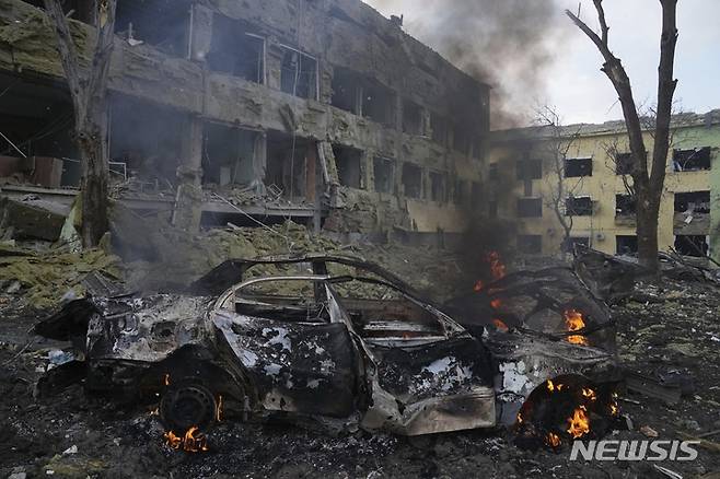 [마리우폴=AP/뉴시스] 9일(현지시간) 우크라이나 마리우폴에 있는 한 산부인과 병원이 러시아군의 포격을 받아 파손된 건물 주변에서 자동차 한 대가 불에 타고 있다. 2022.03.10.