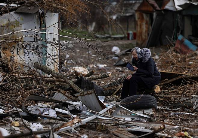 우크라이나 수도 키이우 북서쪽 위성도시 보로댠카에서 지난 8일(현지시간) 한 여성이 러시아군 침공 당시 파괴된 아파트 건물 잔해 속에서 가족의 유품으로 보이는 책을 찾아 살펴보고 있다. / AFP 연합뉴스