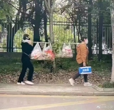 [ 상하이=신화/뉴시스] 상하이 주민 두 사람이 대나무 막대기에 식료품을 걸어 놓고 걸어가고 있다. 2022.5.3   *재판매 및 DB 금지