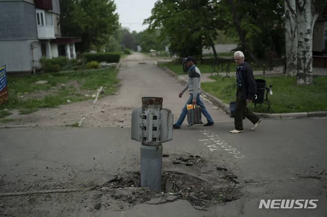 [리시찬스크=AP/뉴시스] 13일(현지시간) 우크라이나 루한스크주 리시찬스크에서 주민들이 도로에 박힌 로켓 주변을 지나고 있다. 2022.05.14.