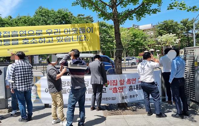 지난 9일 오후 LG광화문빌딩 앞 인도. “어린이집 앞 흡연 그만, 어린이들이 창 밖을 보고 흡연을 흉내냅니다”는 내용의 플래카드 아래에서 직장인들이 담배를 피우는 모습. / 이영관 기자