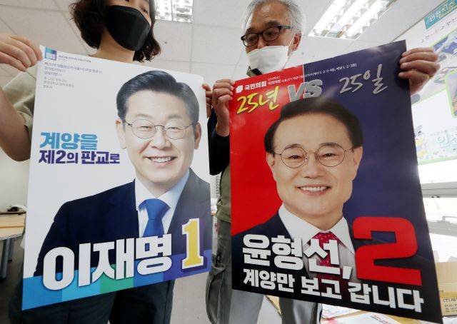 6·1 지방선거운동 개시일을 하루 앞둔 18일 오후 인천시 계양구 계양경기장 선거 벽보 분류 작업장에서 계양구 선거관리위원회 관계자들이 인천 계양을 보궐선거 더불어민주당 이재명 후보와 국민의힘 윤형선 후보의 선거 벽보를 공개하고 있다. 연합뉴스