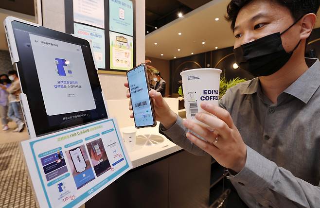 An official from the Ministry of Environment showcases using a barcode label on a disposable cup to receive the deposit back at a coffee shop in central Seoul on May 6. (Joint Press Corps)