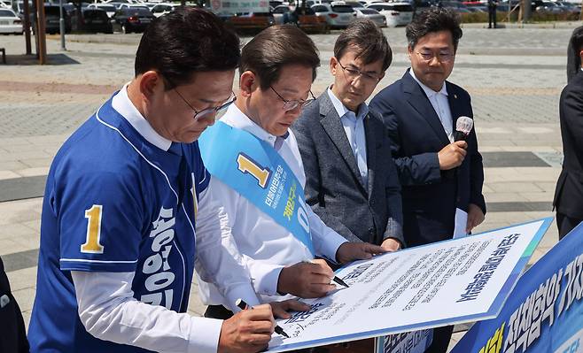 더불어민주당 송영길 서울시장 후보와 이재명 인천 계양을 국회의원 후보가 27일 경기도 김포시 고촌읍 아라 김포여객터미널 아라마린센터 앞 수변광장에서 열린 김포공항 이전 수도권 서부 대개발 정책협약식에서 협약서에 서명하고 있다. /연합뉴스