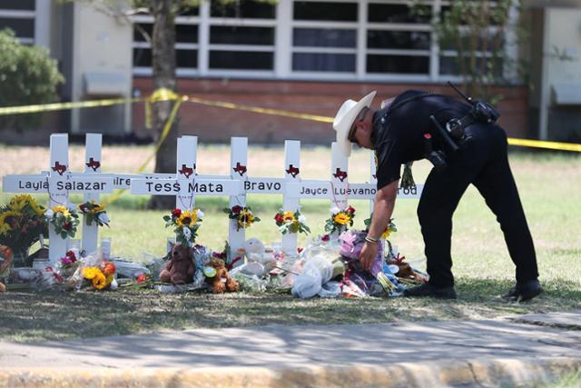 26일 총기 난사 사건이 발생한 미국 텍사스주 소도시 유밸디 초등학교 앞에 한 경찰관이 희생자들을 추모하고 있다. 유밸디=로이터 연합뉴스