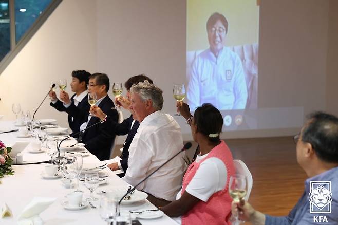 히딩크 감독이 만찬회에서 건배를 하고 있다. 그의 오른쪽에 홍명보 감독이 앉아 있고, 화면에는 영상으로 연결된 황선홍 감독이 보인다. /뉴스1