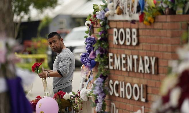 총기 난사 사건이 발생한 미국 텍사스주 유밸디&nbsp;롭초등학교 앞에서 지난 5월 31일(현지시간) 시민이 추모의 꽃을 들고 있다. 18세 범인은 범행에 앞서 사회관계망서비스(SNS)에 총을 쏘겠다고 사전 고지했다. 유밸디=AP연합뉴스