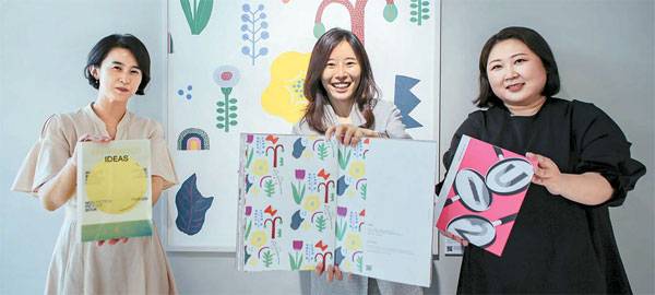 현대어린이책미술관(MOKA) `언-프린티드 아이디어`를 통해 그림책 작가로 활동하는 이수미·이희은 작가(왼쪽부터)와 그들을 지원해온 정동지 MOKA 책임학예사(오른쪽)가 현대L&C에서 제작한 벽지 앞에서 사진촬영을 하고 있다.  [사진 제공 = 현대백화점]