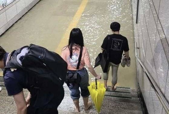 30일 오전 호우특보가 발령된 가운데, 수원시 권선구 1호선 전철 세류역 지하통로가 침수돼 출근길 시민들이 신발을 벗은 채로 걸어가고 있다. [트위터 캡처]