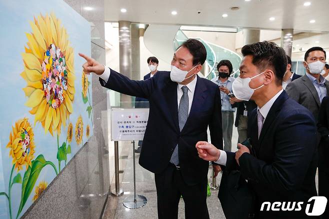 윤석열 대통령이 25일 오전 용산 대통령실에서 출근길 약식 기자회견(도어스테핑)을 마친 뒤 강선아 작가의 '해바라기II' 그림을 둘러보고 있다. 이날 대통령실 1층 양옆 벽면에는 발달장애 작가들의 작품 15점이 처음 전시됐다. 대통령실사진기자단 2022.7.25/뉴스1 © News1 안은나 기자