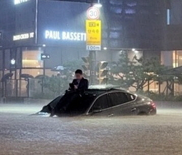 8일 밤 서울의 한 도로가 물에 잠기자 시민이 차체 위로 올라와 있다. 뉴스1