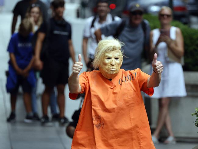 “처벌” : 도널드 트럼프 전 미국 대통령이 지난해 1월 퇴임 이후 처음으로 검찰 조사를 받은 10일, 뉴욕 맨해튼 5번가의 트럼프 타워 앞에서 한 시위자가 트럼프 전 대통령의 얼굴 가면과 죄수복이 연상되는 복장을 착용한 채 트럼프 전 대통령에 대한 처벌을 요구하고 있다. EPA 연합뉴스