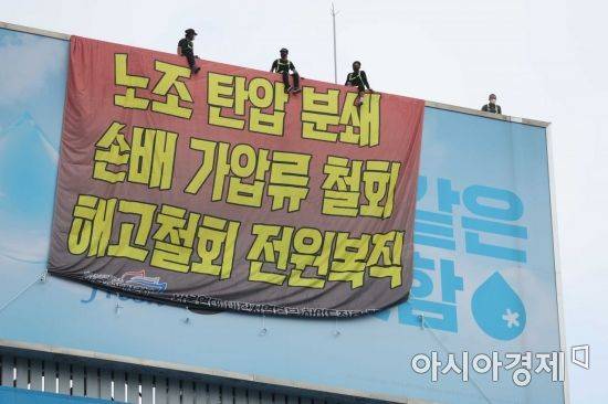 민주노총 공공운수노조 화물연대가 서울 강남구 하이트진로 본사를 점거한 채 사흘째 시위를 이어가고 있는 18일 건물 외벽에 요구사항이 적힌 현수막이 걸려 있다. 노동자들이 옥상 광고판에 올라가 고공 농성을 하고 있다. /문호남 기자 munonam@