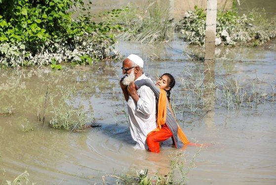 한 할아버지가 28일(현지시간) 파키스탄 차르사다에서 손녀을 등에 업고 홍수로 불어난 길을 걸어가고 있다. 로이터=연합뉴스