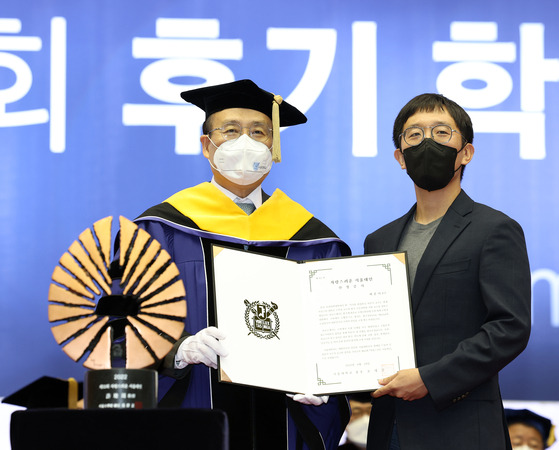 June Huh, right, a Korean-American mathematician and professor of mathematics at Princeton University who became the first person of Korean descent to receive the Fields Medal earlier this year, accepts the "Proud Seoul National University Alumni" award from the university's president Oh Se-jung during the graduation ceremony held on the campus in Gwanak District, southern Seoul, on Monday. [YONHAP]