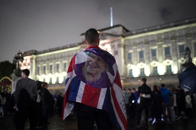 8일 영국 런던 버킹엄궁 앞에서 한 시민이 엘리자베스 2세 여왕 사진이 붙어있는 유니언잭을 두르고 있다. 런던=AP 연합뉴스