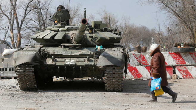 지난 3월18일(현지시간) 러시아가 포위한 우크라이나 남부 항구도시 마리우폴에서 한 주민이 러시아군 탱크 옆을 지나가고 있다. 마리우폴|로이터연합뉴스