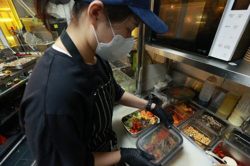 직원이 배달 음식을 다회용기에 담고 있다. [사진 출처 = 연합뉴스]
