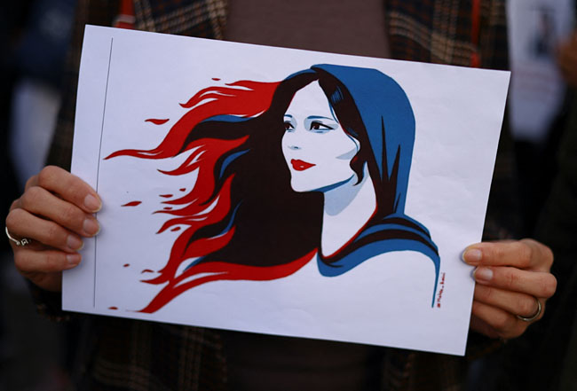 23일(현지시간) 독일 베를린 브란덴부르크 문 앞에서 열린 이란 ‘히잡 미착용 여성 의문사’ 사건 항의 시위에서 한 참석자가 의문사 희생자 마샤 아미니를 형상화한 그림을 들고 있다. 로이터 연합뉴스