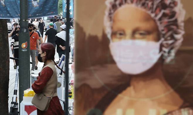 25일 서울 명동거리에서 마스크 쓴 모나리자 그림 뒤로 시민들이 지나가고 있다. 뉴스1
