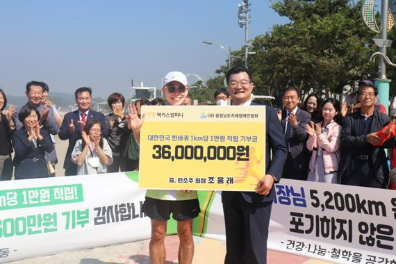 국내 최초로 대한민국 한바퀴 5200㎞ 마라톤에 도전중인 ㈜맥키스컴퍼니 조웅래회장(왼쪽)이 29일 충남 보령에 도착, 이건휘 충남지체장애인협회장에게 1㎞당 1만원씩 모은 적립금 3600만원을 기부하고 있다.